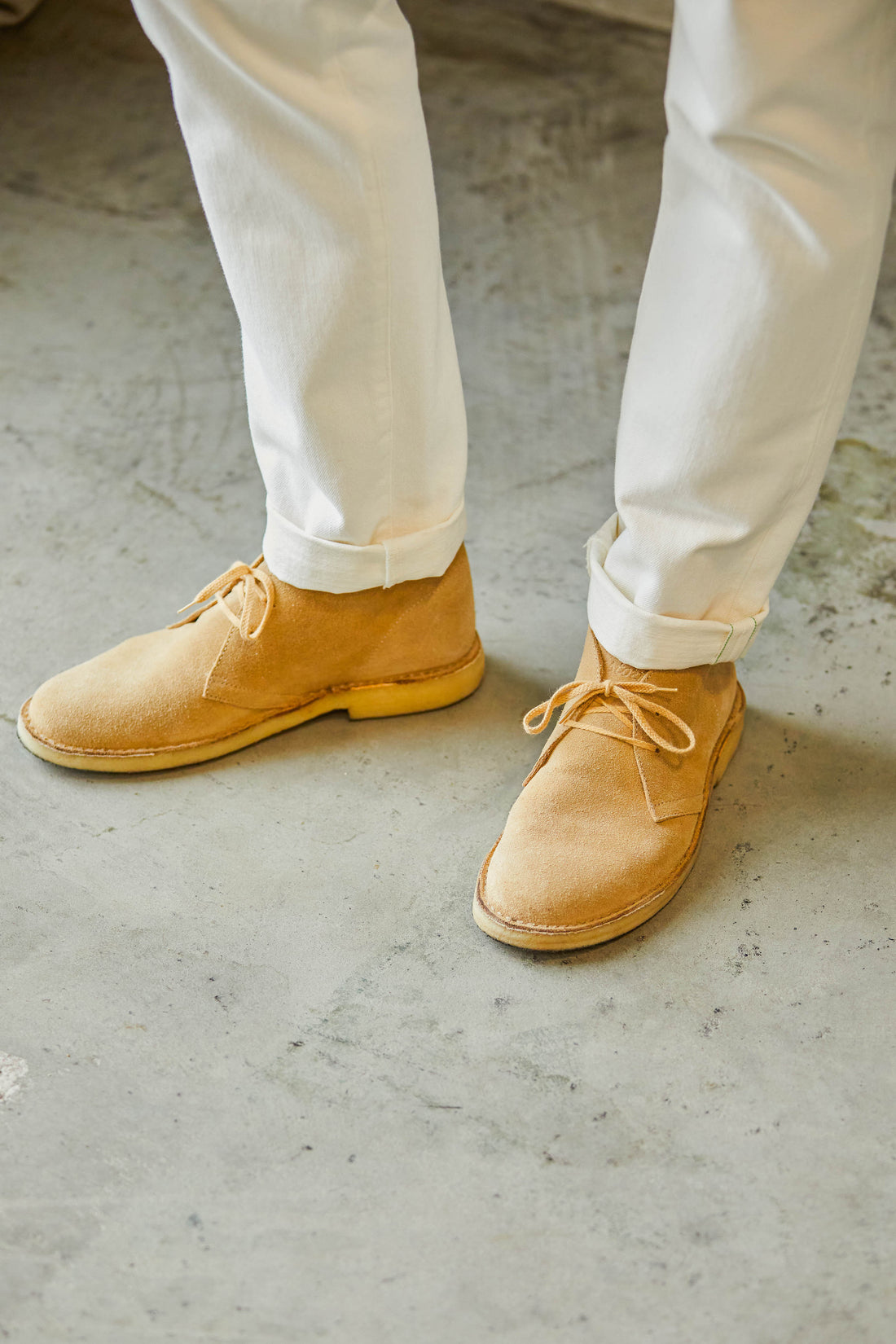 A person wearing tan suede shoes and white pants standing on a concrete surface.