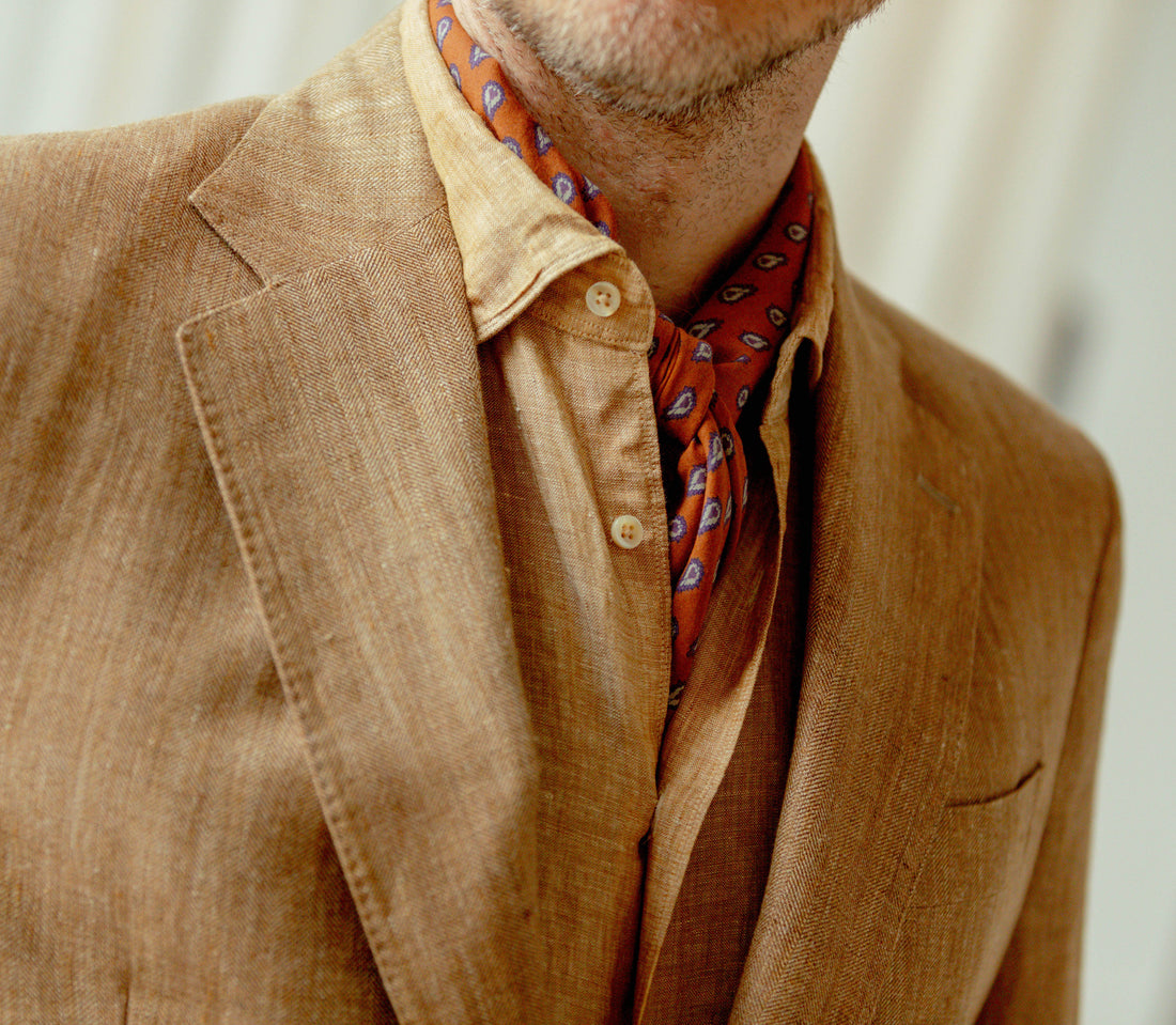 A man wearing a brown jacket and a red patterned scarf.