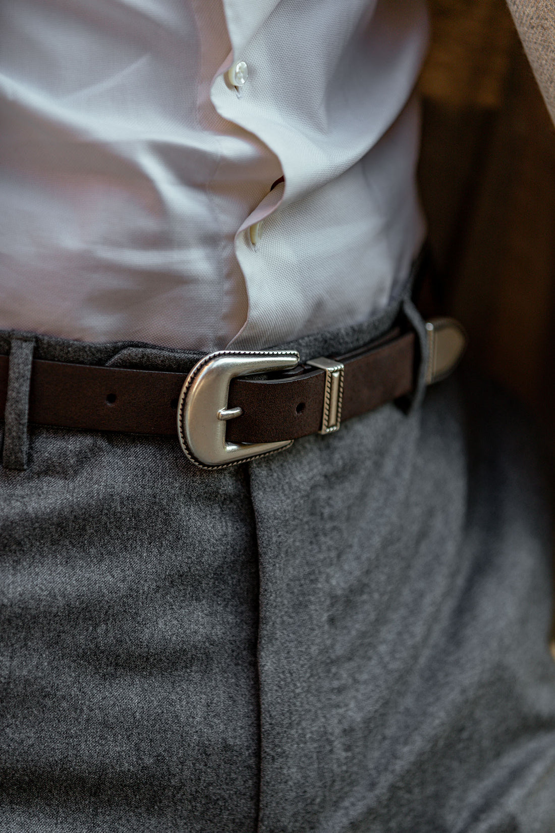 A close-up of a person wearing a white shirt tucked into gray trousers, secured with a brown leather belt.