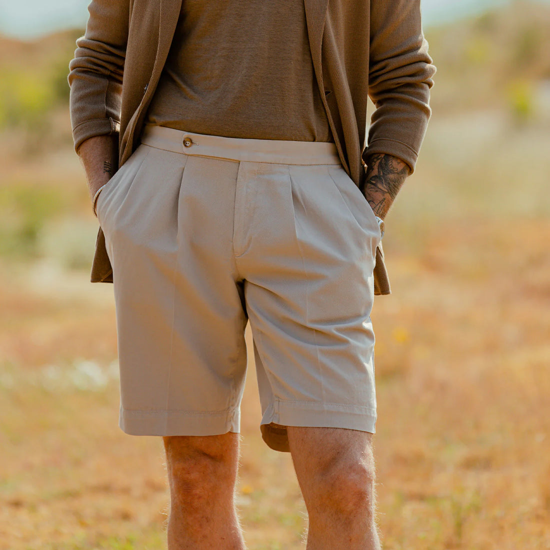 A man standing outdoors wearing a brown jacket and beige shorts.