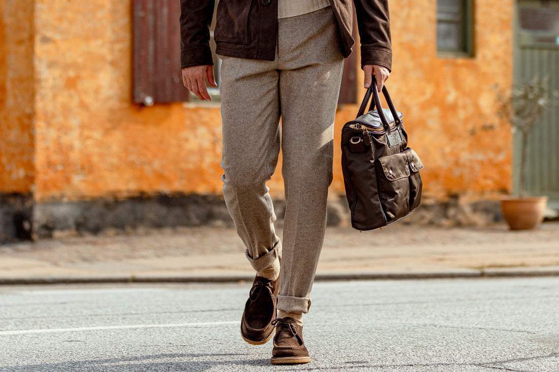 A person in business casual attire carrying a leather bag while walking across the street.