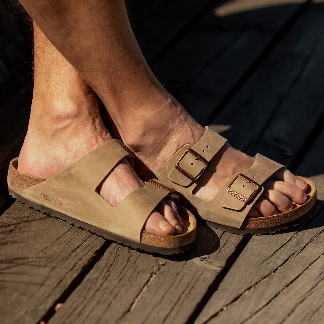 A pair of feet wearing birkenstock sandals on a wooden surface.