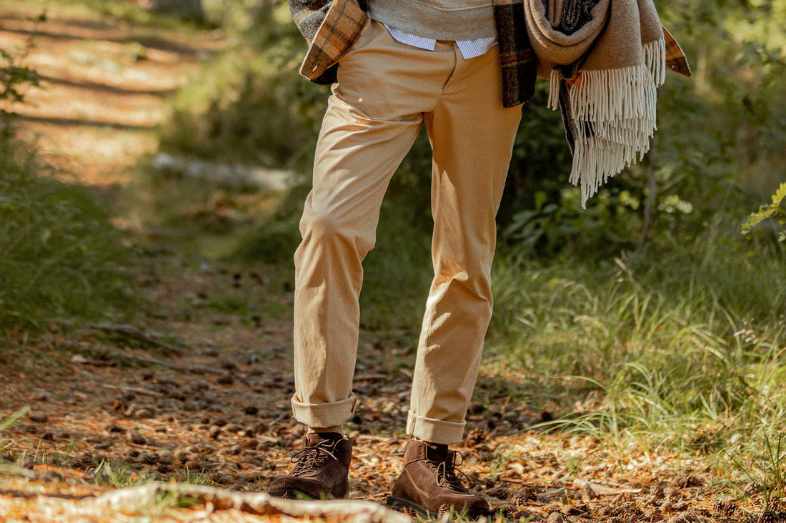A person wearing khaki pants and brown boots carries a plaid blanket while walking in a forest.