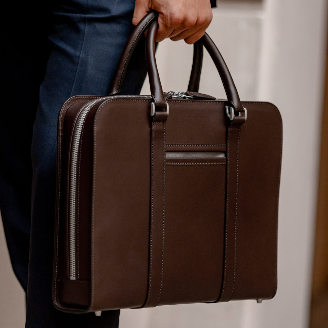 A person in formal attire holding a brown leather briefcase.