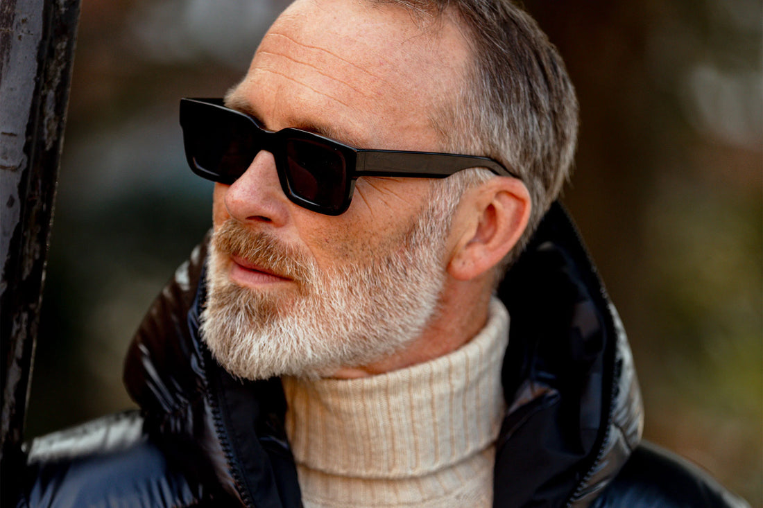 Bearded middle-aged man wearing sunglasses and a turtleneck, looking thoughtfully to the side.