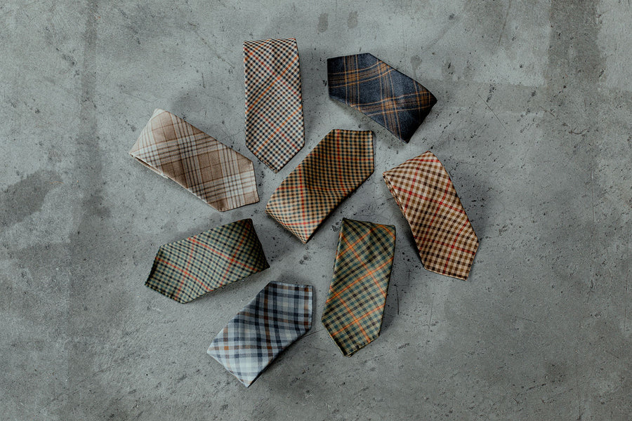 A collection of folded plaid fabrics arranged in a pattern on a gray concrete surface.