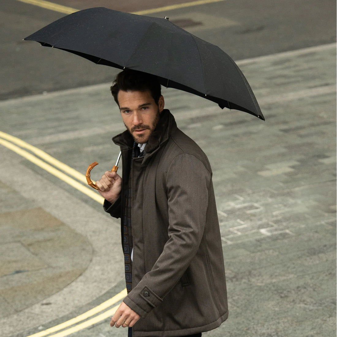 Man holding an umbrella walking on a street.