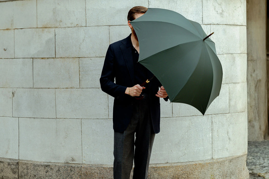 A person in a suit partially obscured by an open green umbrella against a curved wall.
