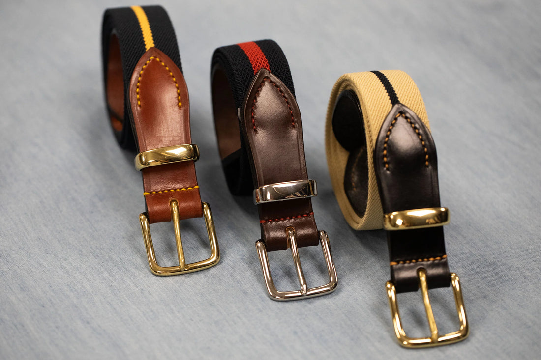 Three rolled-up leather belts with metal buckles on a textured surface.