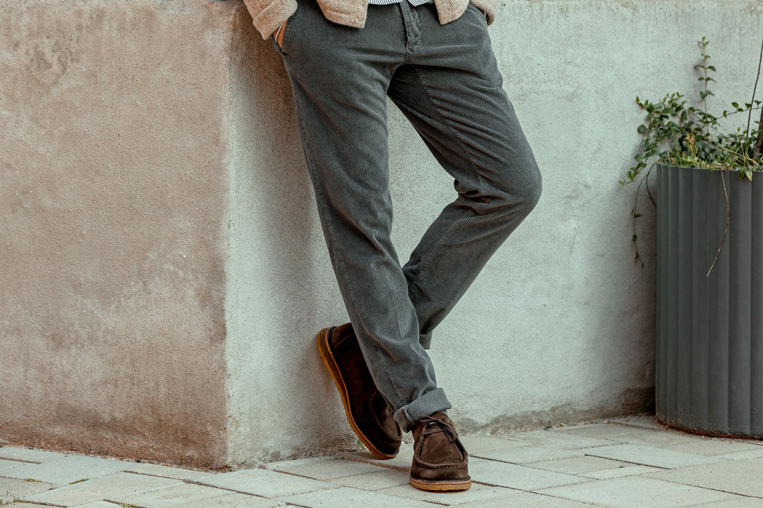Person leaning against a wall showcasing casual trousers and brown shoes.