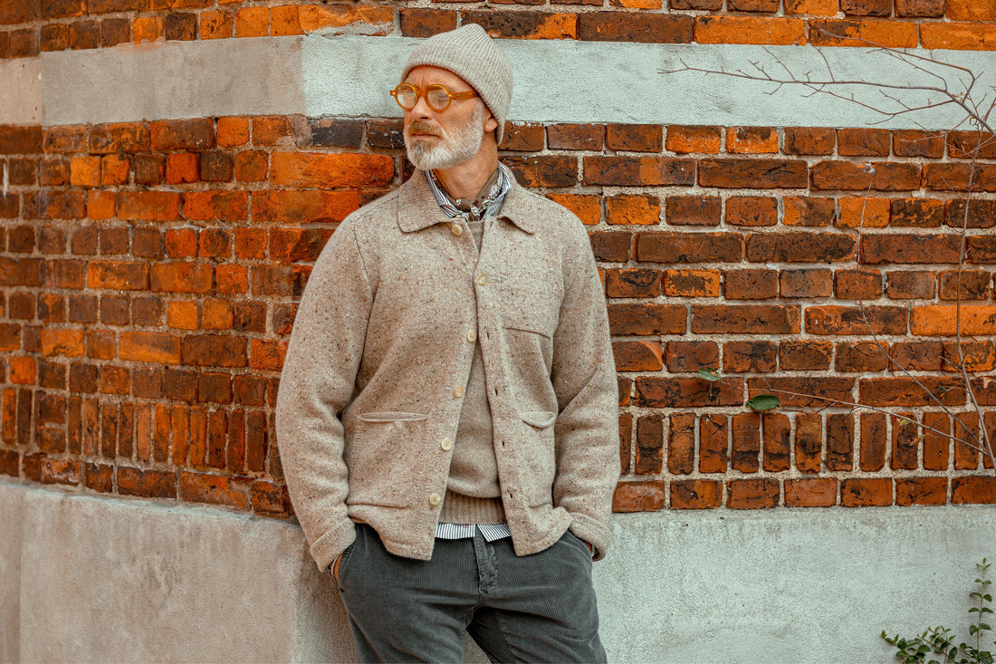 A man in a woolen cap and jacket standing against a brick wall.