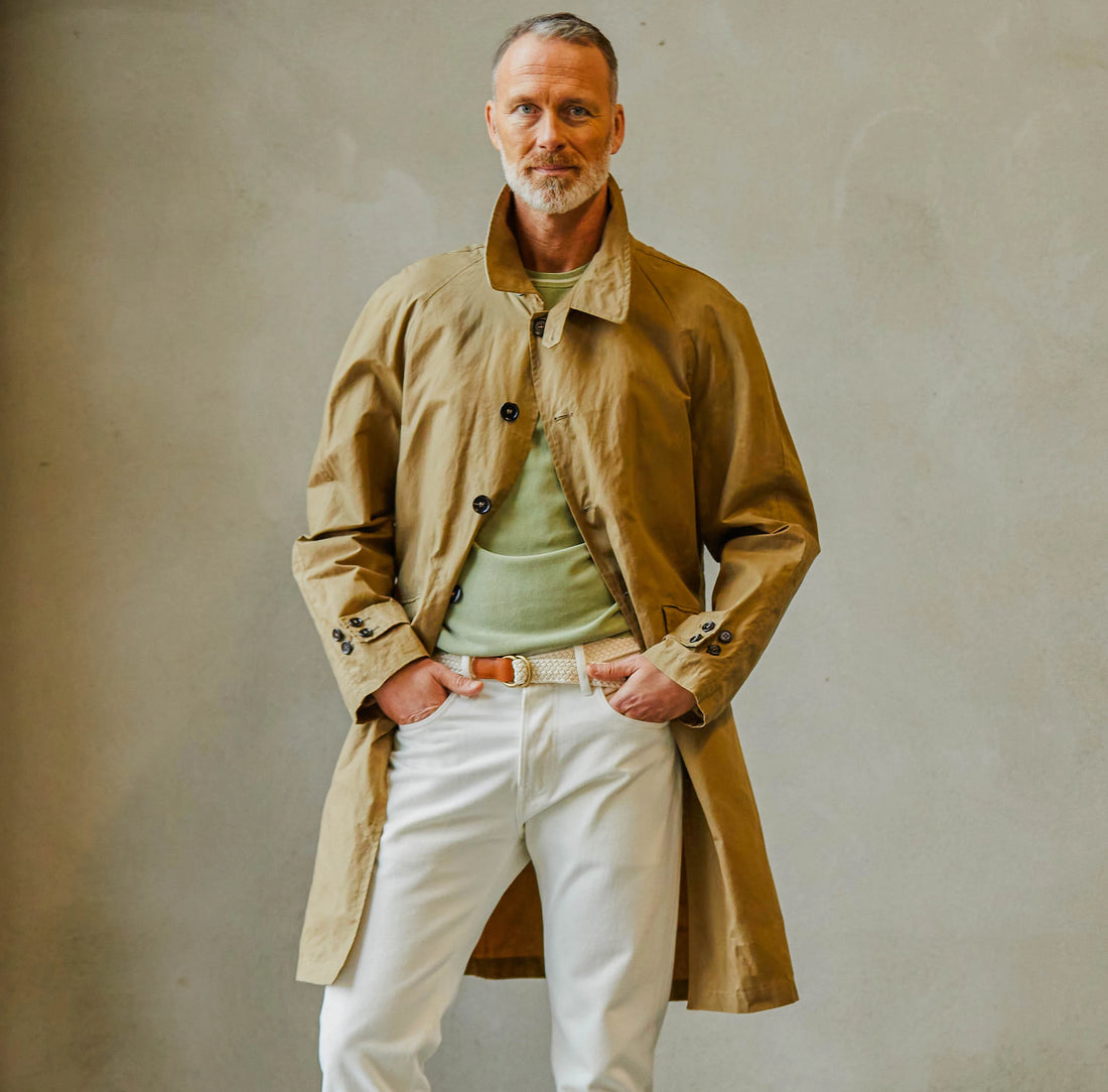 A confident middle-aged man dressed in smart casual attire with a trench coat, standing against a neutral background.
