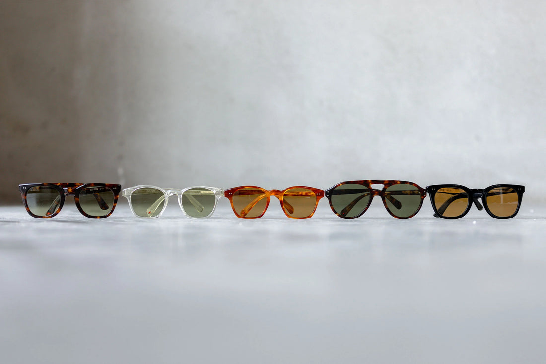 Row of assorted sunglasses on a reflective surface against a gray background.