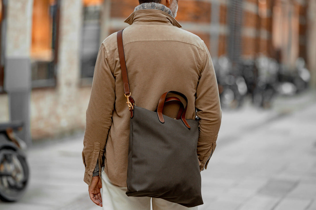 A person walking outdoors with a brown shoulder bag and sunglasses.