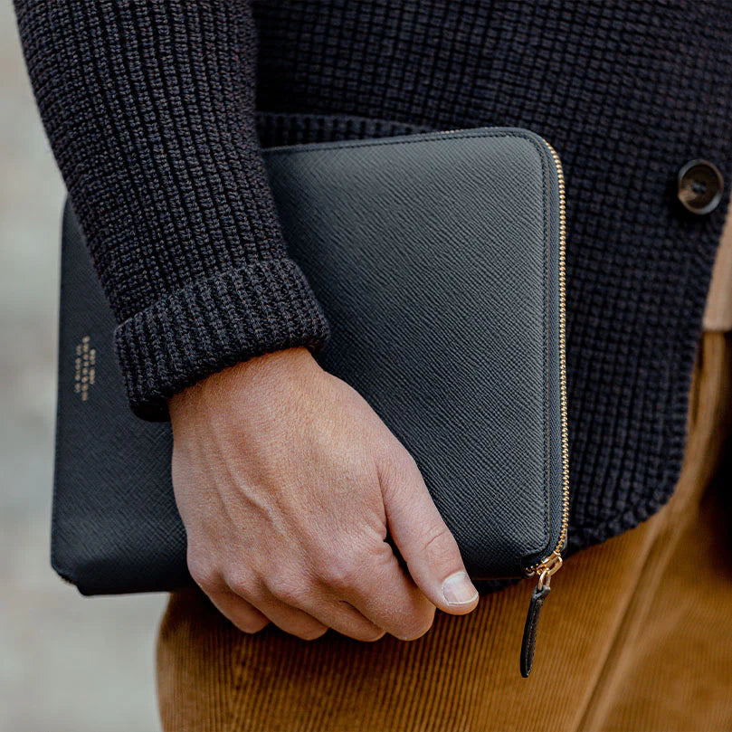 A person wearing a dark sweater holds a small gray zippered pouch.