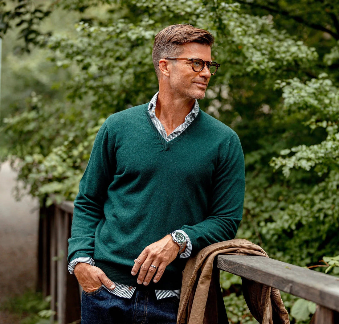Man in glasses leaning on a wooden railing outdoors with a thoughtful expression.