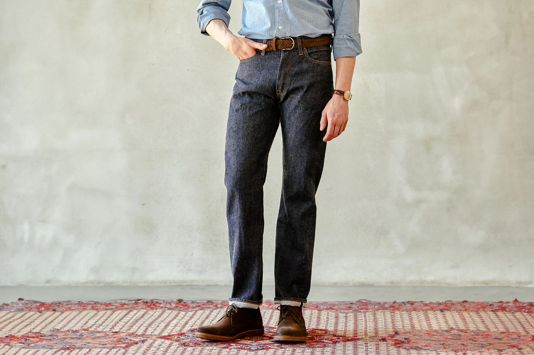 Person standing with hands in pockets wearing denim jeans and brown boots.