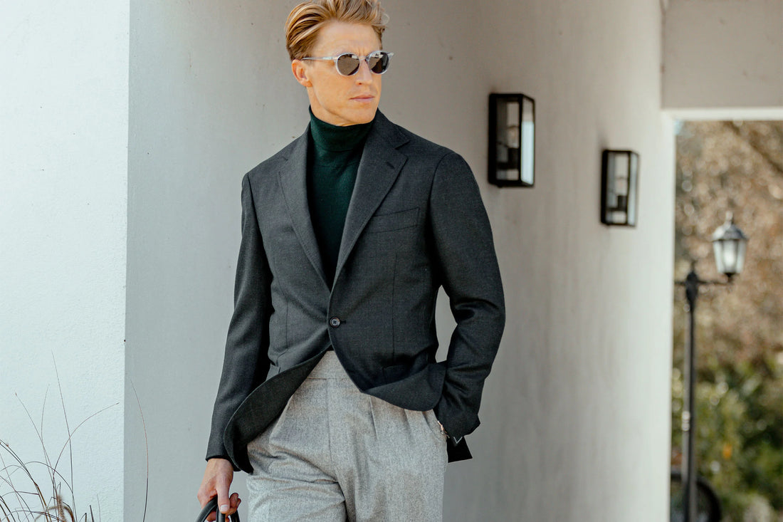A man in stylish business attire with a blazer and turtleneck standing confidently outdoors.