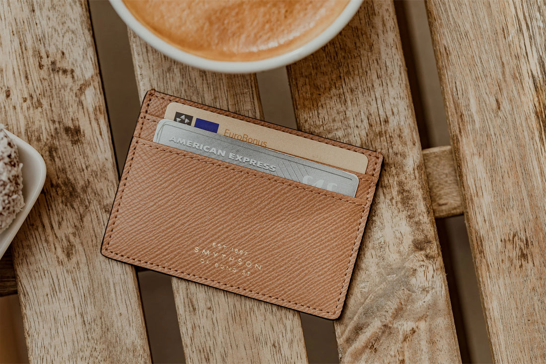 A leather wallet with credit cards on a wooden table next to a cup of coffee.