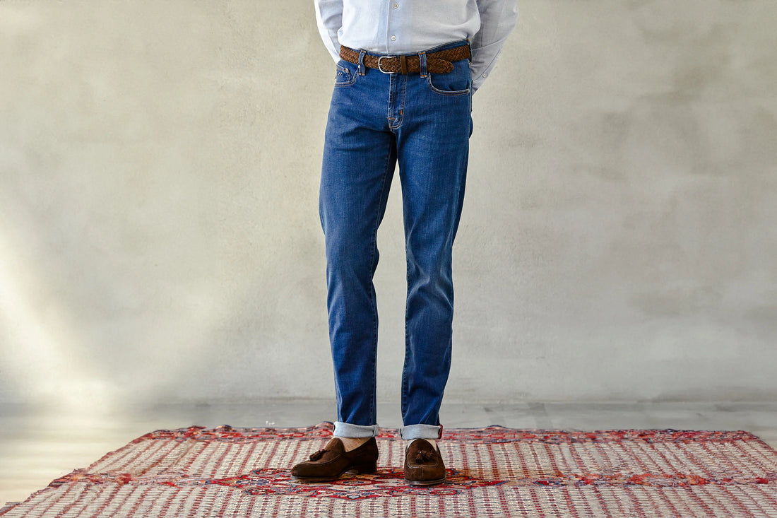 A person wearing blue jeans and brown shoes stands on a red patterned rug against a neutral background.