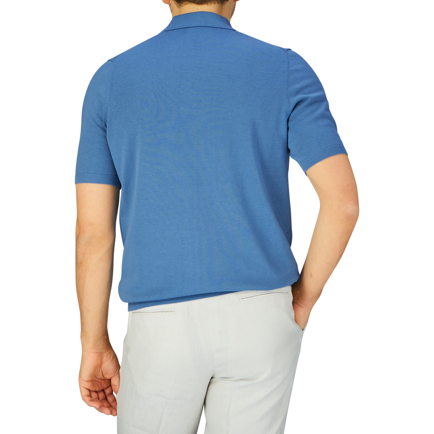 Man wearing an Alan Paine airforce blue knitted cotton polo shirt and white pants, viewed from the back.