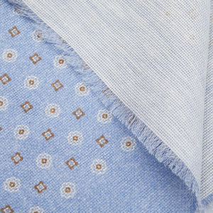 Close-up of a Amanda Christensen sky blue medallion printed cotton linen scarf with a floral pattern and a frayed edge over a striped textile.
