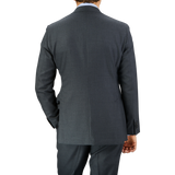 Rear view of a man wearing a tailored Baltzar Sartorial Grey Super 100's Wool Suit Jacket and pants, standing against a plain light grey background.