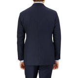 Rear view of a man wearing a Baltzar Sartorial Navy Super 100's Wool Suit Jacket and matching pants, against a grey background.