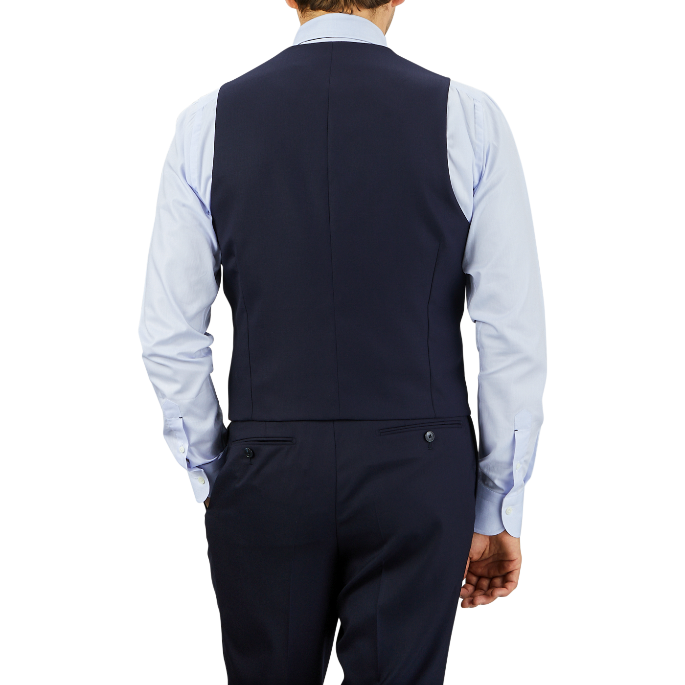 A man viewed from behind wearing a Baltzar Sartorial Navy Super 100s Wool DB Waistcoat and matching trousers with a light blue shirt, standing against a gray background.