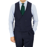 Man in a tailored Baltzar Sartorial Navy Super 100s Wool DB Waistcoat, white shirt, dark tie, and matching trousers, standing against a gray background.