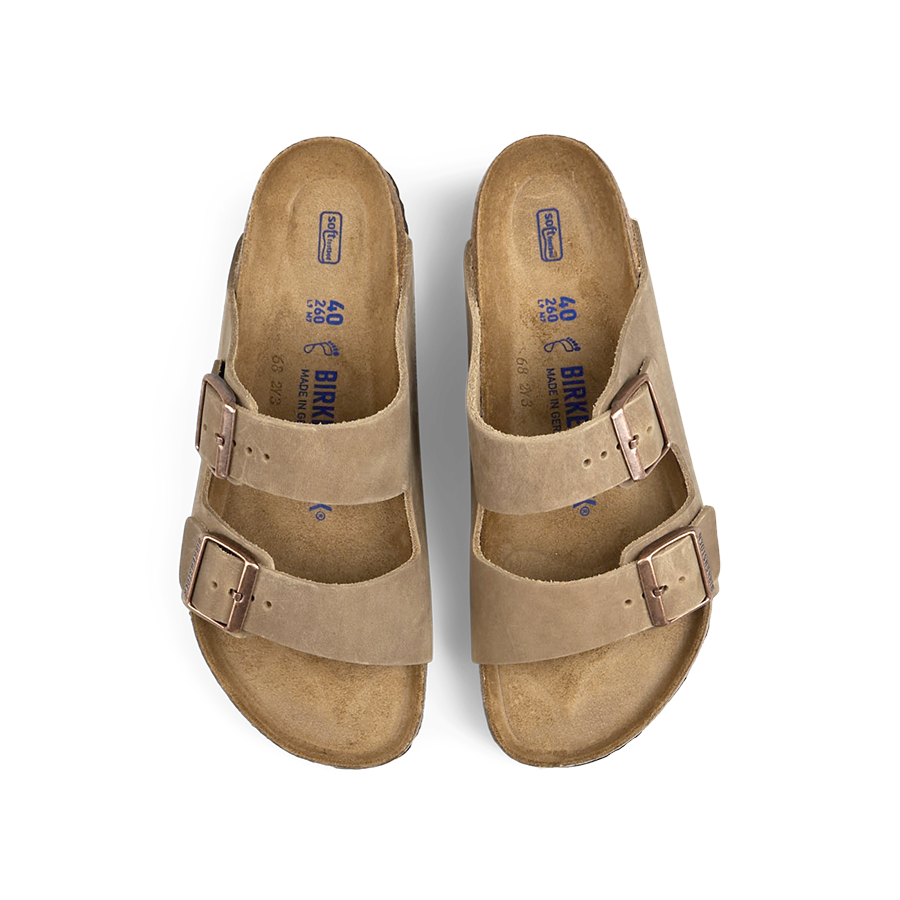 A pair of Tabacco Brown Natural Leather Birkenstock Arizona sandals with buckles on a transparent background.