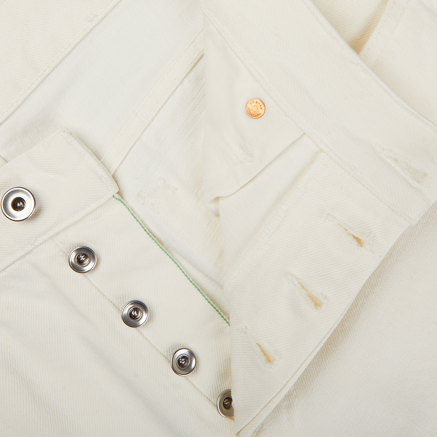 Close-up of a white Ecru Stone Washed Kuroki Cotton M5 Jeans garment with a gold button and multiple silver snap fasteners by C.O.F Studio.