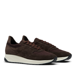 A pair of dark brown suede leather CQP Stride Runners with white soles on a translucent background.