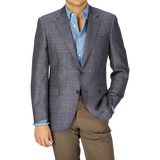 A man in a Canali Blue Gingham Checked Wool Silk Linen Blazer and light blue shirt paired with beige trousers, cropped at the chest, against a grey background.