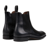 A pair of sleek black leather Simpson Chelsea boots with brown lining and pull tabs on a white background, crafted by expert craftsmen.