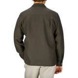 Rear view of a man wearing a De Bonne Facture Arabica Green Linen Canvas Painter's Jacket and light beige pants, standing against a light gray background.