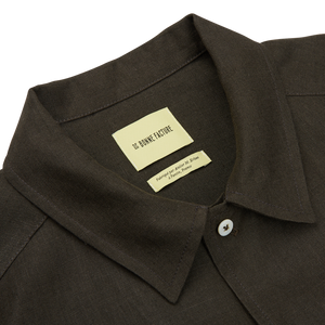 Close-up of a De Bonne Facture Arabica Green Linen Canvas Painter's Jacket with a white label inside the collar reading "le chicke future. property of jonah maraq stean.