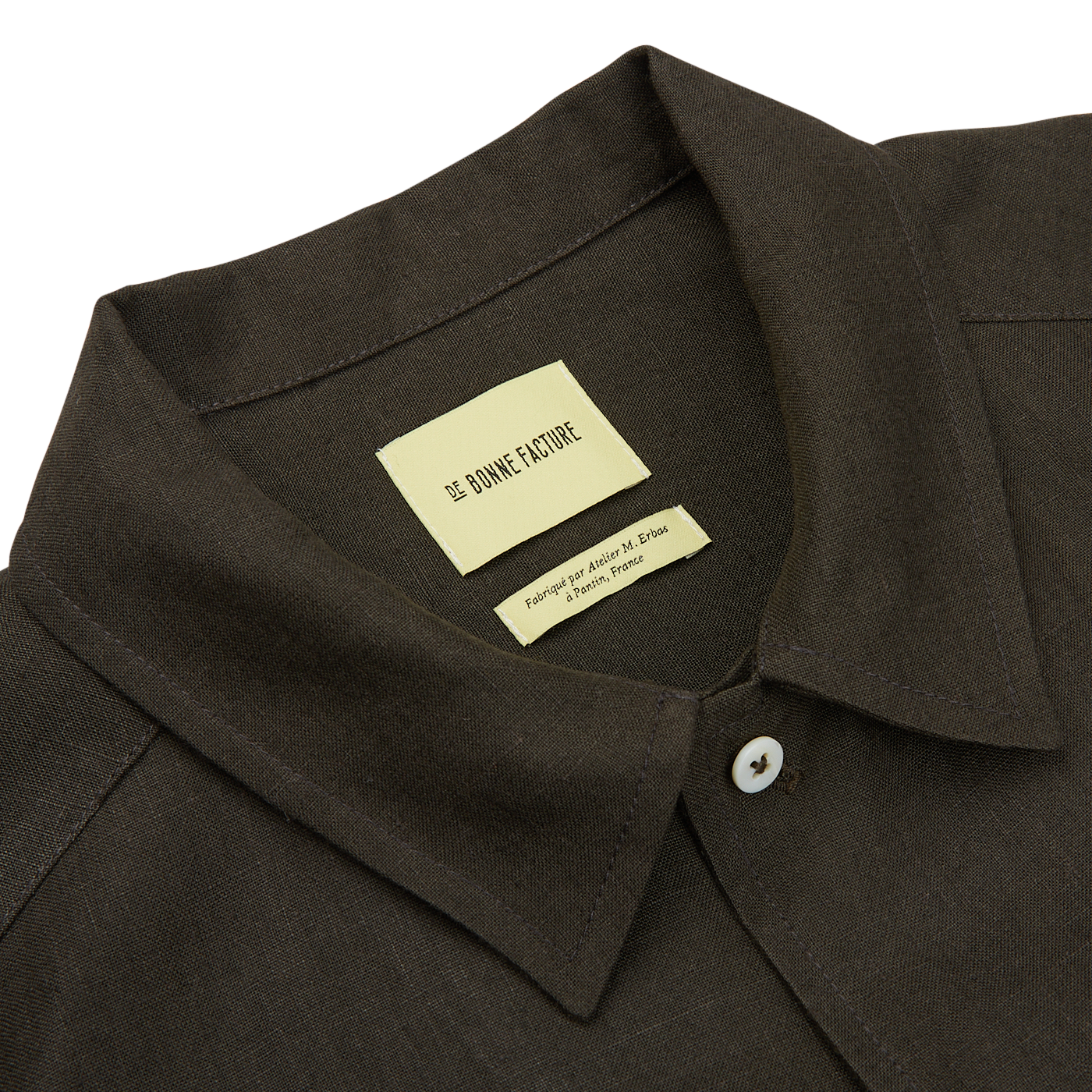 Close-up of a De Bonne Facture Arabica Green Linen Canvas Painter's Jacket with a white label inside the collar reading "le chicke future. property of jonah maraq stean.