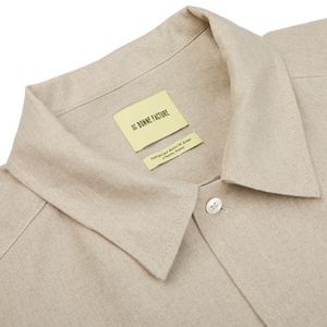 Close-up of a De Bonne Facture oatmeal beige linen canvas painter's jacket collar with a sewn-in label reading "le bonheur toute".
