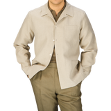 A man dressed in a Oatmeal Beige Linen Canvas Painter's Jacket by De Bonne Facture and green trousers standing against a light background.
