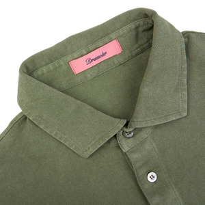 Close-up of a grass green cotton piquet polo shirt with a pink label showing the brand name "Drumohr" inside the collar.