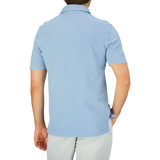 Rear view of a man wearing a light blue, short-sleeved Drumohr Sky Blue Cotton Piquet Polo Shirt and light-colored trousers against a plain background.