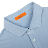 Close-up view of a light blue Drumohr Sky Blue Cotton Piquet polo shirt with a collar and a branded orange label.