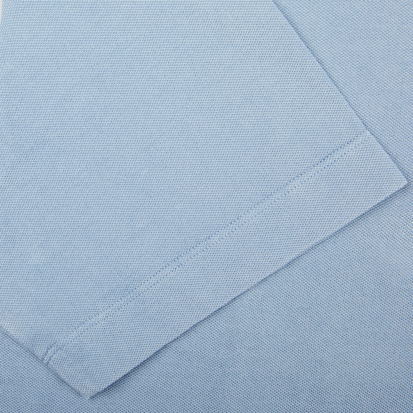 Close-up of a sky blue Drumohr cotton piquet polo shirt texture with a stitched seam, made in Italy.