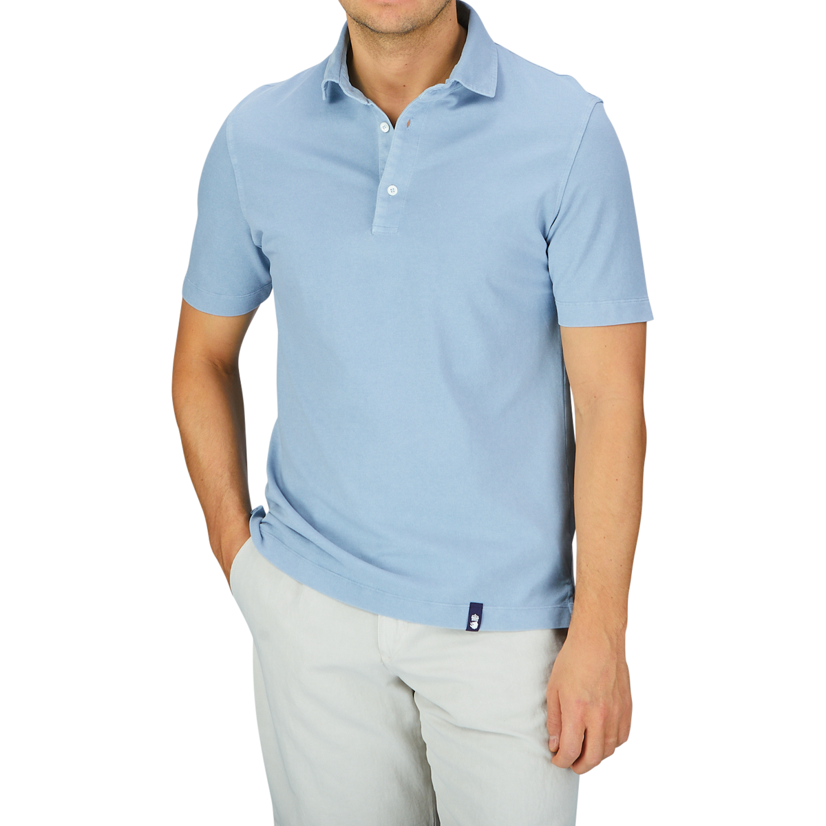 A man wearing a light blue Drumohr Sky Blue Cotton Piquet Polo Shirt and white pants against a grey background.