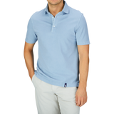 A man wearing a light blue Drumohr Sky Blue Cotton Piquet Polo Shirt and white pants against a grey background.