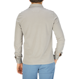 The back view of a man wearing a Fedeli Taupe Beige Organic Cotton LS Polo Shirt and blue pants.