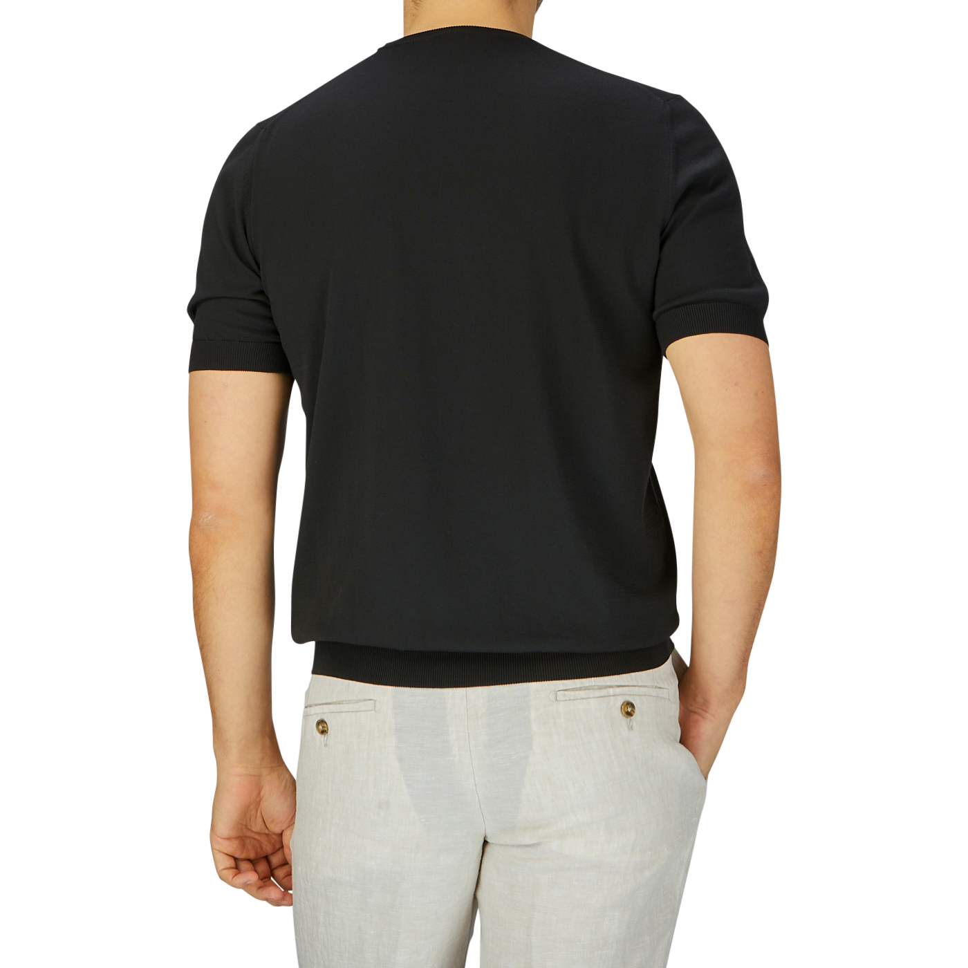 Rear view of a man in a Gran Sasso black organic cotton t-shirt and light beige pants against a grey backdrop.