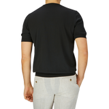 Rear view of a man in a Gran Sasso black organic cotton t-shirt and light beige pants against a grey backdrop.