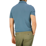 Rear view of a man in a Turquoise Fresh Cotton Mesh Polo Shirt by Gran Sasso and green trousers, standing against a neutral background.
